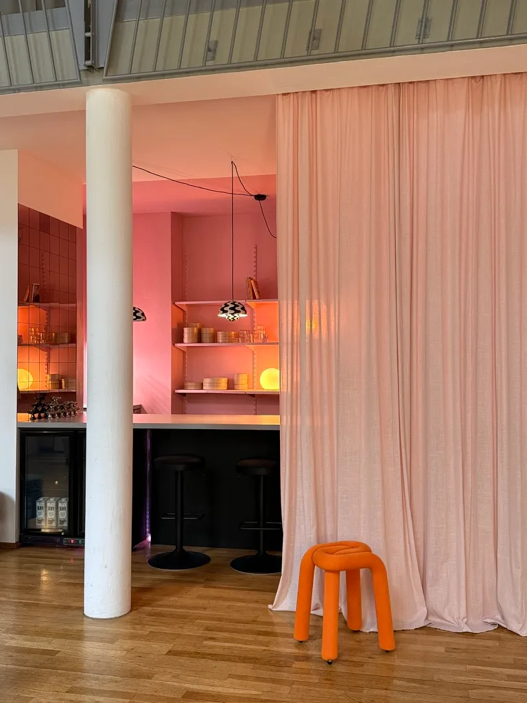 Küche mit rosa Wand, blauem Vorhang und orangem Hocker